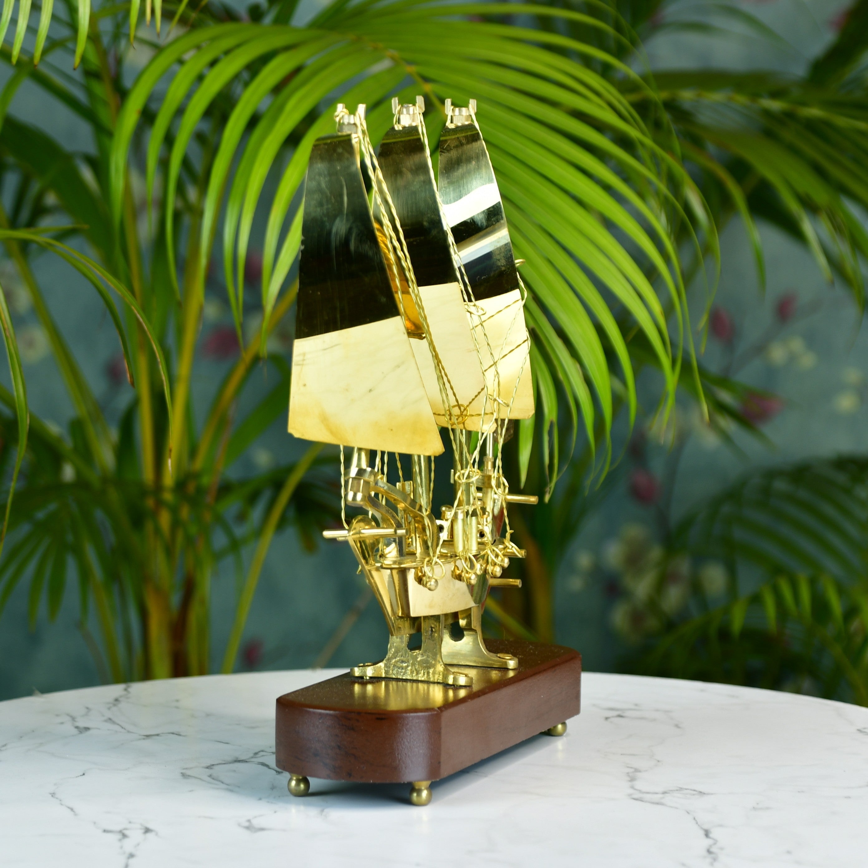 MAYII brass ship decor tabletop with polished brass sails on wooden base against green plant background