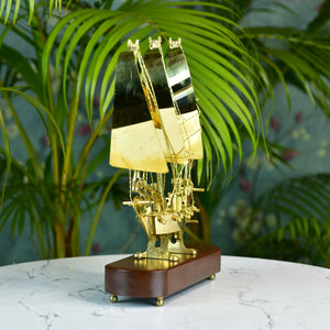 MAYII brass ship decor tabletop with polished brass sails on wooden base against green plant background